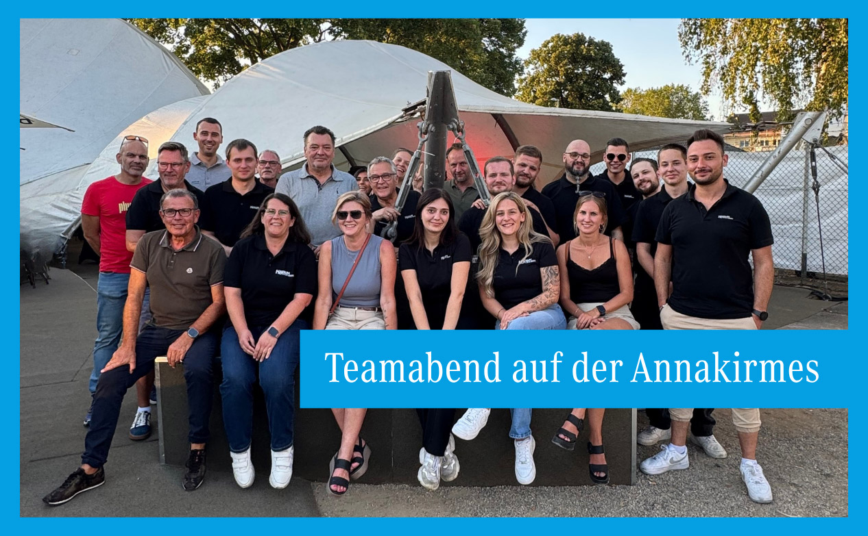 Gruppe von etwa 20 Personen in Freizeitkleidung vor weißen Zelten bei Tageslicht mit blauem Schriftbanner 'Teamabend auf der Annakirmes'